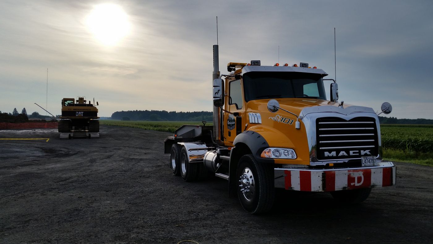 Camion Mack jaune de Danis Construction sur un chantier au lever du jour